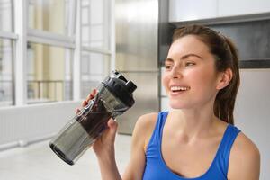 ritratto di sportiva potabile acqua durante allenarsi sessione nel vivente camera, fa sua fitness formazione esercizi a casa foto