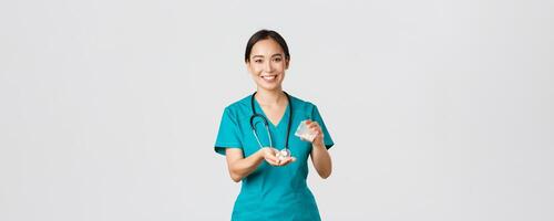 assistenza sanitaria lavoratori, prevenire virus, quarantena campagna concetto. sorridente amichevole asiatico femmina medico, medico nel strofina, dare paziente medicazione a partire dal contenitore, bianca sfondo foto