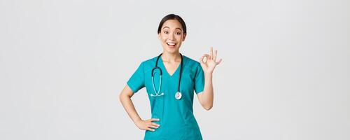 covid19, assistenza sanitaria lavoratori, pandemia concetto. sorpreso e contento asiatico femmina medico, infermiera nel scrub mostrando va bene gesto e sorridente stupito, lode simpatico opera, essere d'accordo con qualcuno foto