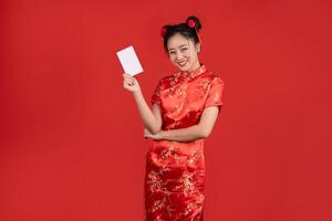 contento giovane asiatico donna indossare rosso cheongsam Tenere credito carta isolato su rosso sfondo. contento Cinese nuovo anno foto
