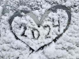 il nuovo anno è 2024. un' cuore dipinto su il parabrezza di un' auto coperto con fresco Natale neve. foto