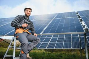 ritratto di sorridente fiducioso ingegnere tecnico con elettrico Cacciavite, in piedi nel davanti di incompiuto alto esterno solare pannello foto voltaico sistema