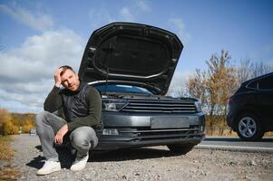 uomo riparazione un' rotto auto di il strada. uomo avendo guaio con il suo rotto auto su il autostrada ciglio della strada. uomo guardare sotto il auto cappuccio. auto pause giù su il autostrada. ciglio della strada assistenza concetto. foto