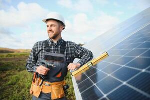 ritratto di sorridente fiducioso ingegnere tecnico con elettrico Cacciavite, in piedi nel davanti di incompiuto alto esterno solare pannello foto voltaico sistema