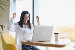 ragazza gioisce nel vincente avendo sollevato sua mani su seduta nel davanti di portatile.ragazza seduta nel bar, orologi in linea gli sport incontro su computer. foto