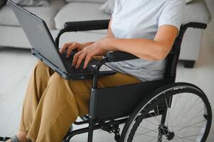 positivo anziano donna nel sedia a rotelle Lavorando su computer portatile, esso libero professionista, in linea foto