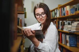 nel il biblioteca - bella femmina alunno con libri Lavorando nel un' alto scuola biblioteca. foto