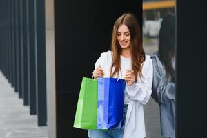 alla moda bellissimo contento donna in piedi con shopping borse vicino un' shopping centro su nero venerdì. foto