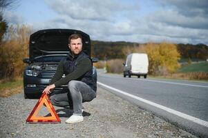 un' giovane uomo con un' nero auto quello rotto giù su il strada, copia spazio. foto