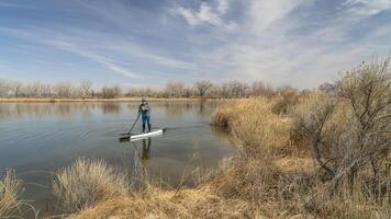 anziano maschio paddler è paddling In piedi su paddleboard su un' calma lago nel presto primavera scenario nel Colorado foto