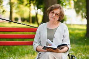 pensionato donna lettura un' libro su il panchina foto