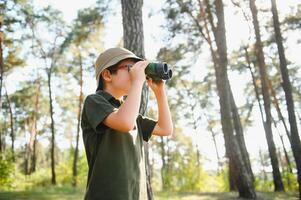 poco ragazzo esploratore con binocolo durante escursioni a piedi nel autunno foresta. concetti di avventura, scoutismo e escursioni a piedi turismo per bambini. foto