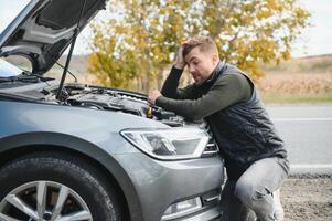 uomo riparazione un' rotto auto di il strada. uomo avendo guaio con il suo rotto auto su il autostrada ciglio della strada. uomo guardare sotto il auto cappuccio. auto pause giù su il autostrada. ciglio della strada assistenza concetto. foto