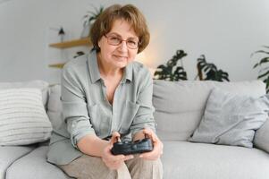 più vecchio persona avendo divertimento giocando un' consolle con un' video gioco seduta su il divano. foto