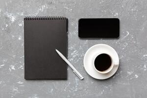 moderno ufficio scrivania tavolo con taccuino, smartphone e altro forniture con tazza di caffè. vuoto taccuino pagina per voi design. superiore Visualizza, piatto posare foto