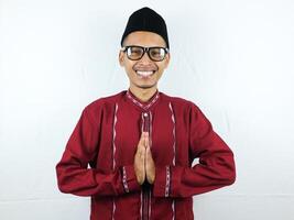 asiatico musulmano uomo indossare bicchieri sorridente per dare saluto durante Ramadan e eid al Fitr celebrazione al di sopra di bianca sfondo foto