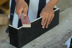 mani di un' falegname manualmente levigatura di legno con carta vetrata nel un' la lavorazione del legno o carpenteria laboratorio foto