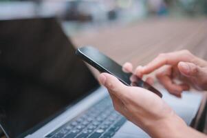 un' uomo d'affari o libero professionista utilizzando computer il computer portatile e smartphone seduta su tavolo al di fuori Lavorando su attività commerciale o Internet in linea marketing foto