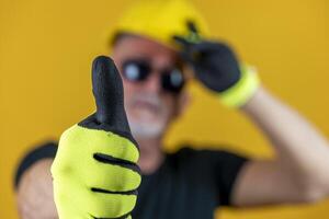 lavoratore con guanti e casco mostrando pollice su contro giallo sfondo foto