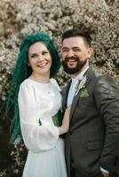un' barbuto sposo giochi e un' ragazza con verde capelli contro il sfondo di fioritura primavera foto