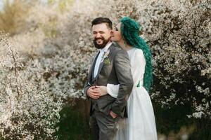 un' barbuto sposo giochi e un' ragazza con verde capelli contro il sfondo di fioritura primavera foto