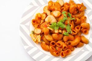 maccheroni pasta con pomodoro salsa e affettato salsiccia servito su un' bianca piatto su un' blu sfondo. foto