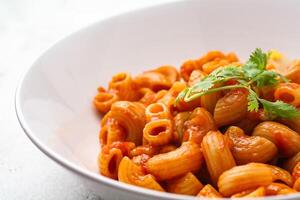 maccheroni con pomodoro salsa e prezzemolo nel un' bianca ciotola servito su un' bianca piatto foto