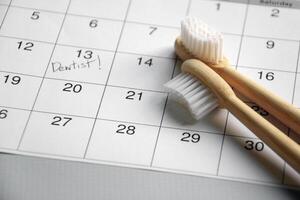 su un' leggero grigio sfondo, Là è un' calendario con un' dal dentista Nota e spazzolini da denti. foto