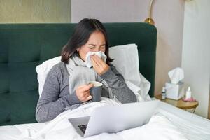 donna con freddo, avendo influenza, soggiorno nel letto, starnuti nel tovagliolo, che cola naso e influenza sintomi foto