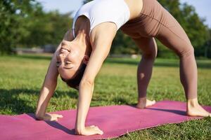 donna sorridente mentre fabbricazione ponte asana, fare yoga nel parco su gomma da cancellare stuoia foto