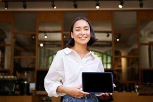 allegro giovane ristorante amministratore, asiatico ragazza Spettacoli digitale tavoletta e sorridente foto