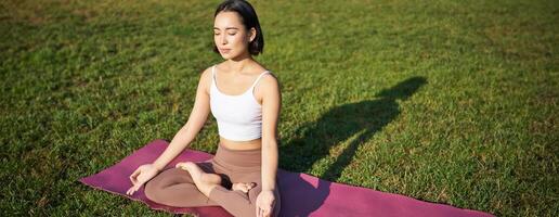 consapevolezza e meditazione. giovane asiatico donna sorridente mentre fare yoga, rilassante nel asana su gomma da cancellare stuoia, fare esercizi nel parco su fresco aria foto