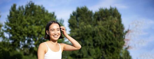 meditazione e consapevolezza. giovane asiatico donna sorridente su fitness stuoia nel parco, fare yoga addestramento, Meditare su fresco aria foto