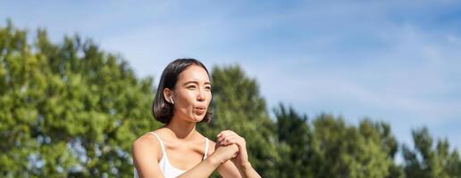 asiatico fitness ragazza fare squat nel parco, utilizzando resistenza gruppo musicale, allungamento yoga corda per allenarsi formazione su fresco aria foto