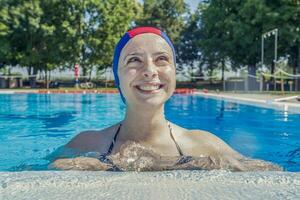 bella ragazza indossare un' piscina berretto a il bordo piscina spruzzi wate foto