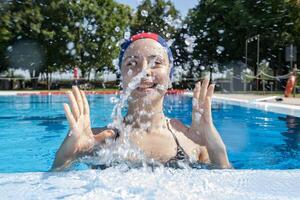 bella ragazza indossare un' piscina berretto a il bordo piscina spruzzi wate foto