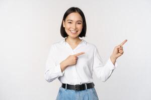 ritratto di bellissimo asiatico donna, commessa puntamento dita giusto e mostrando Informazioni, bandiera o logo, vendita annuncio, in piedi al di sopra di bianca sfondo foto