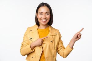contento asiatico donna sorridente, puntamento dita Giusto, invitante per dai un'occhiata su saldi, mostrando annuncio pubblicitario bandiera o logo, in piedi al di sopra di bianca sfondo foto