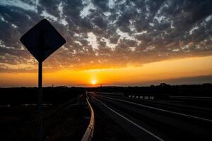 incredibilmente bellissimo tramonto nel il campagna. luminosa pesca e arancia tramonto e cumulo nuvole nel il cielo. tramonto su il autostrada, il ombra di il strada cartello. foto