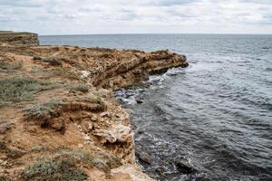 un' vicino tiro di un' mare mantello, onde battito contro rocce, di spessore mare schiuma. riflusso e maree. camminare di il mare costa su un' nuvoloso offuscare giorno. foto