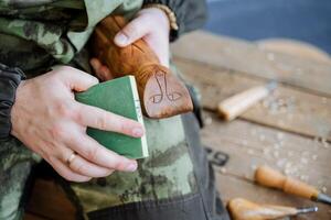 un' uomo nel un' camuffare uniforme ossequi il superficie di un' di legno giocattolo. souvenir fatto di legna nel il modulo di un' gatto. in lavorazione legna e la creazione di giocattoli a partire dal esso. foto