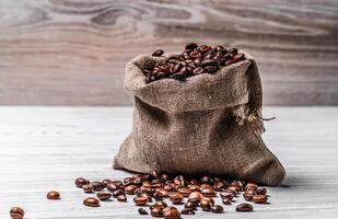 piccolo tela ruvida Borsa pieno di fresco arrostito arabica fagioli e alcuni semi dire bugie su il tavolo. sacco con Marrone naturale robusta cereali su il leggero superficie. foto