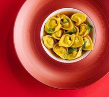 pieno tortellini con erbe aromatiche su rosso piatto foto