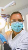 paziente pov visitare dentale clinica per chirurgia trattamento influenzato messa. medico e infermiera Lavorando insieme nel moderno ortodontico ufficio, illuminazione il lampada e l'esame persona indossare protezione maschera. foto