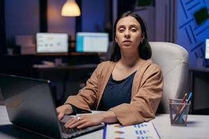 donna d'affari Tenere mani su il computer portatile tastiera guardare a telecamera. inteligente donna seduta a sua posto di lavoro nel il corso di in ritardo notte ore fare sua lavoro. foto