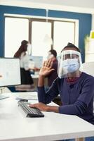 pov di africano lavoratore nel remoto chiamata nel posto di lavoro seduta a scrivania indossare viso maschera contro covid19. donna A proposito di con squadra durante in linea conferenza mentre colleghi Lavorando nel sfondo. foto