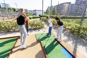 carino scuola ragazza giocando mini golf con famiglia. contento bambino piccolo bambino avendo divertimento con all'aperto attività. estate sport per bambini e adulti, all'aperto. famiglia vacanze o ricorrere. foto