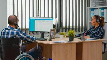 paralizzato uomo d'affari nel sedia a rotelle utilizzando cuffia fabbricazione teleappuntamento e offerta cliente sostegno. immobilizzato Disabilitato libero professionista Lavorando nel finanziario aziendale edificio utilizzando moderno tecnologia foto