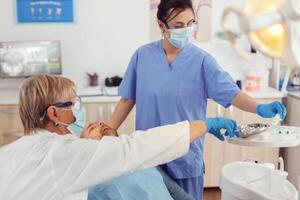 ospedale squadra Lavorando a dentale chirurgia analizzando eh Salute utilizzando stomatologiche utensili Lavorando nel medico clinica ufficio. uomo paziente in attesa su odontoiatria sedia durante stomatologia consultazione foto