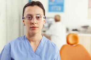 vicino su di donna infermiera nel uniforme guardare in telecamera mentre Lavorando nel stomatologia ospedale ufficio. medico squadra in attesa malato paziente per inizio dentale chirurgia durante stomatologiche appuntamento foto